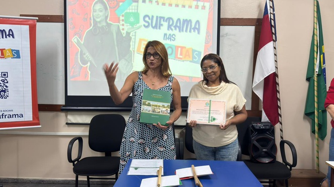 Duas mulheres, a da esquerda falando, a da direita com um certificado na mão