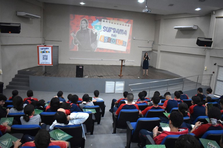 Foto mostra mulher palestrando em auditório lotado