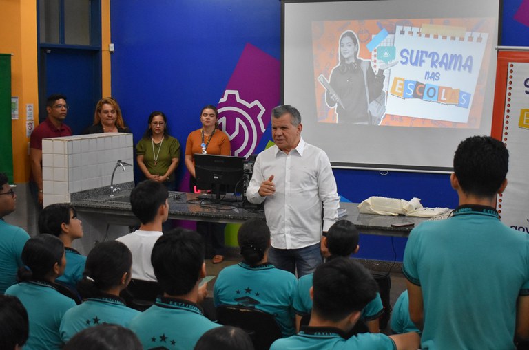 Foto mostra homem de blusa branca fazendo uma explanação a um grupo de estudantes