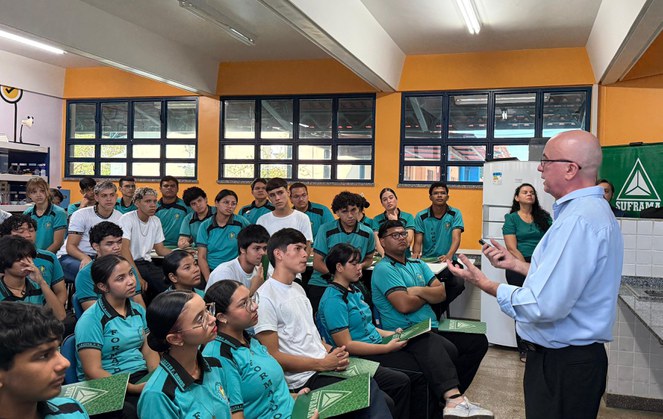 Foto mostra homem em pé de blusa azul falando a estudantes