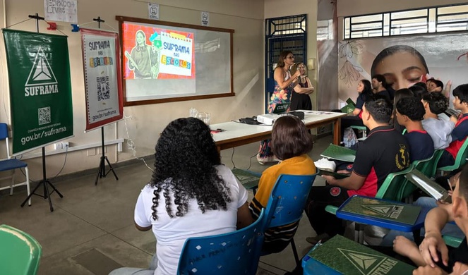 Foto mostra mulher falando ao microfone para grupo de alunos