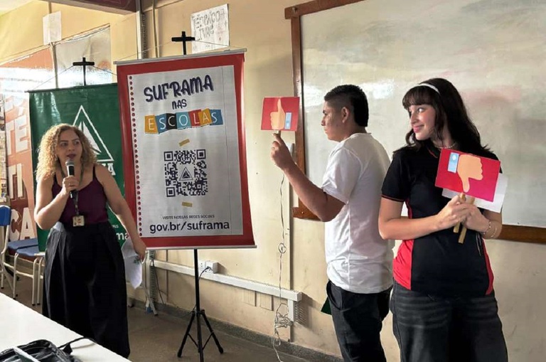 Foto mostra dois jovens segurando duas placas e uma mulher observando com microfone na mão
