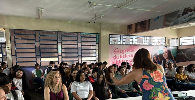 Foto mostra grupo de pessoas sentadas numa sala e observando a explanação feita por uma mulher em pé