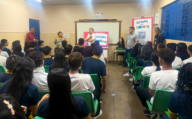 Foto mostra homem de blusa branca falando a um grupo de pessoas em uma sala de aula
