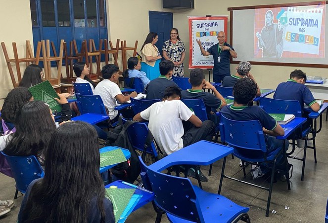 Foto mostra homem vestido de blusa azul, com duas mulheres ao lado dele e um banner ao fundo