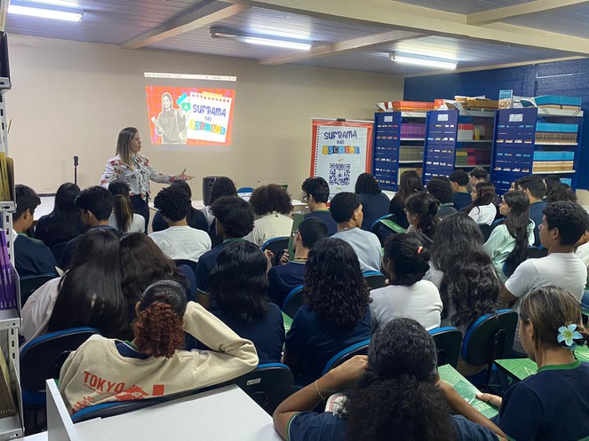 Foto mostra mulher em pé fazendo uma explanação a um grupo de estudantes