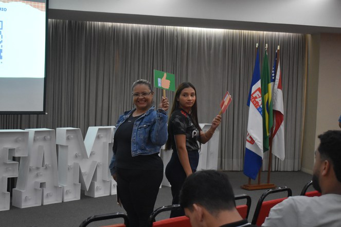 Foto mostra dois jovens segurando uma plaquinha, como parte de uma dinâmica após palestra realizada