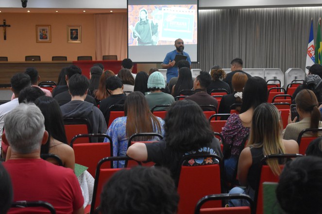 Foto mostra homem em pé falando em auditório lotado