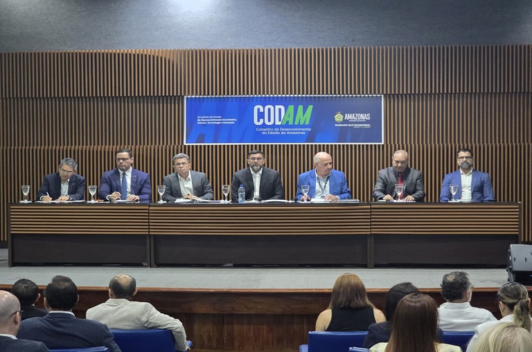 Imagem em um auditório lotado com sete pessoas na mesa principal