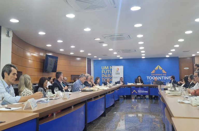 Foto mostra pessoas à mesa em uma reunião