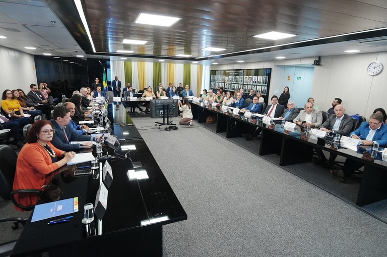 Foto mostra reunião institucional com um grupo de pessoas sentadas