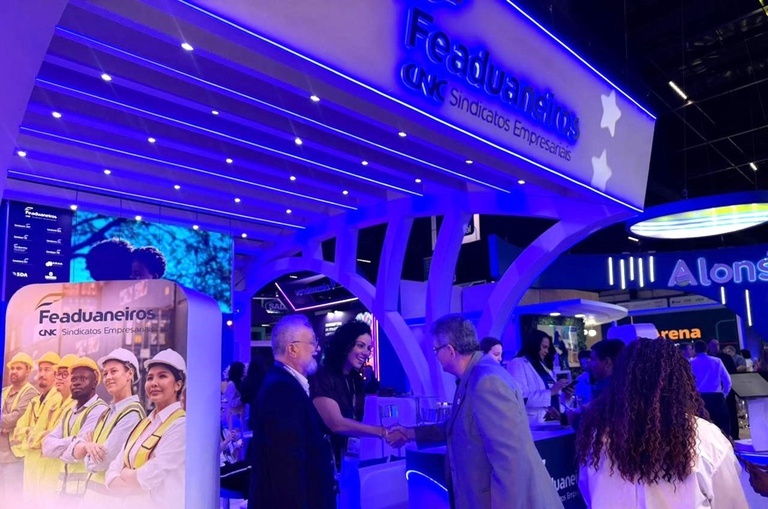 Fotos mostra mulher apertando a mão de um homem, observada por outro homem em um estande