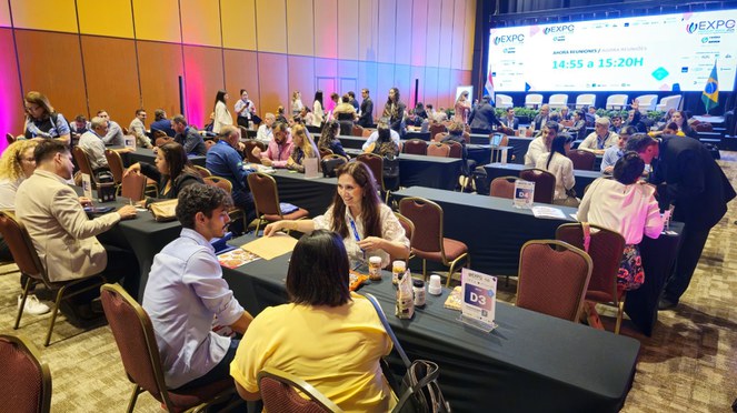 Foto mostra pessoas reunidas num grande evento, com um painel ao fundo