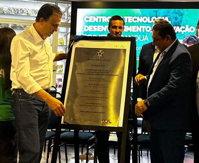 Foto mostra homens observando placa de inauguração, após descerramento