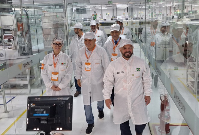 Foto mostra pessoas caminhando numa fábrica com jalecos e toucas brancos