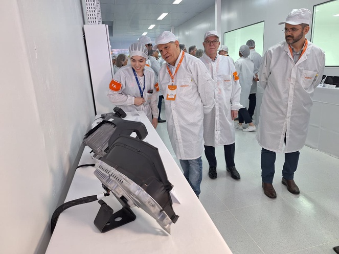 Foto mostra homem de jaleco e boné branco observando um equipamento
