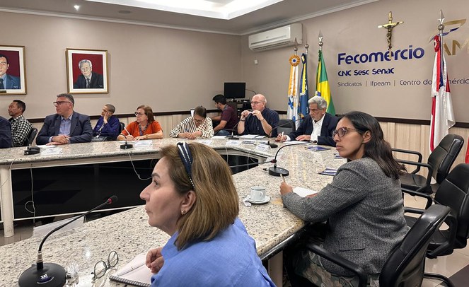 Foto mostra pessoas olhando atentamente para uma explicação, com uma cruz e bandeiras ao fundo