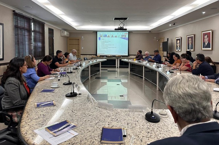 Foto mostra grupo de pessoas sentadas e olhando para um telão