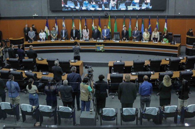Foto mostra pessoas reunidas em um evento público, entoando o Hino Nacional Brasileiro