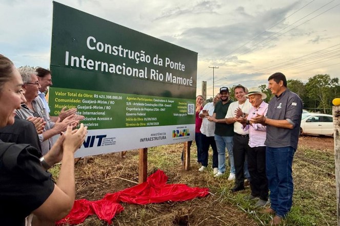 Foto mostra pessoas em frente a uma placa