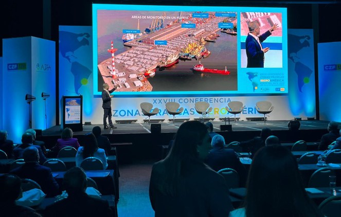 Foto mostra homem palestrando com o apoio de um telão em um auditório lotado