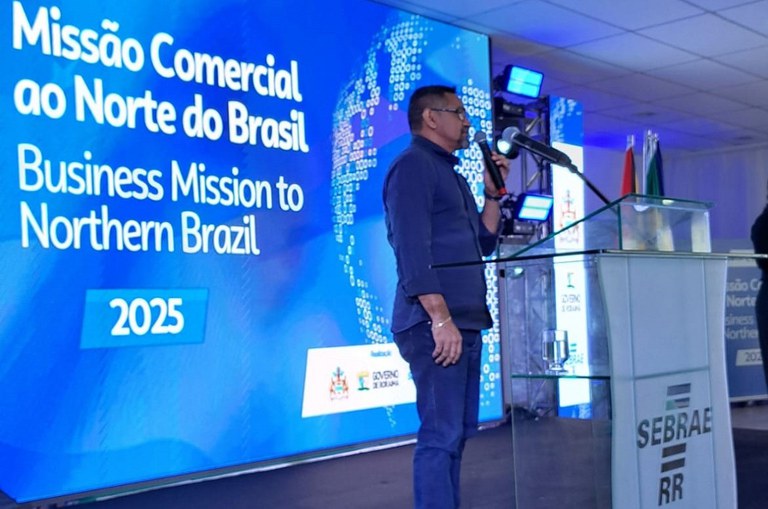 Foto mostra homem com microfone na mão falando em evento público