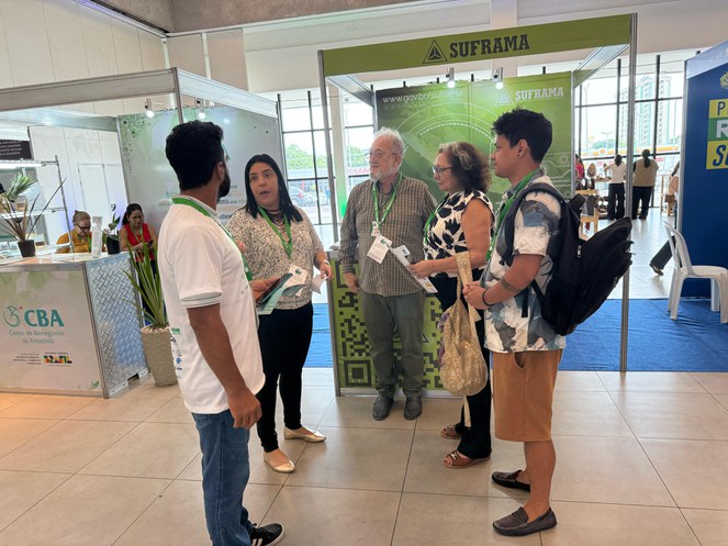 Foto mostra homem de blusa marrom observando uma mulher conversando com homem de barba