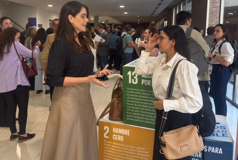 Foto mostra mulher de sai bege e blusa preta em conversa com outra mulher de blusa branca
