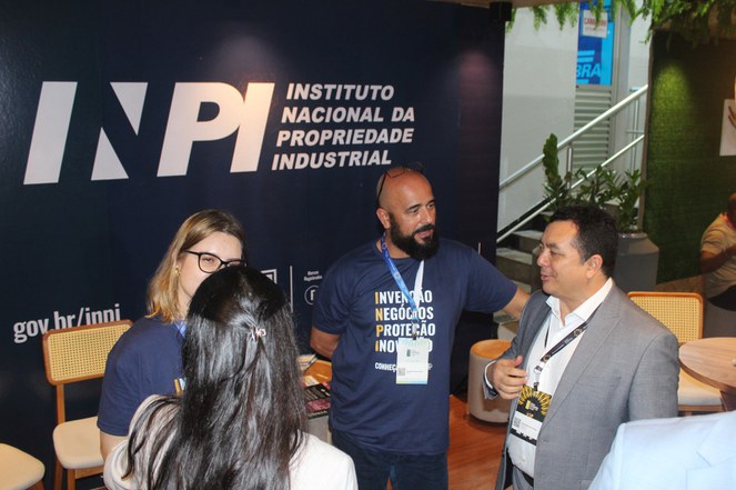 Foto mostra homem com blazer cinza em conversa com outro homem de blusa azul