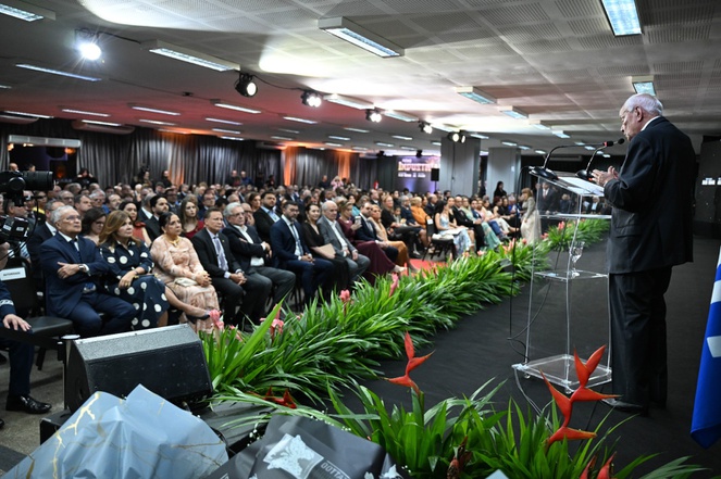 Foto mostra homem em pé falando ao microfone para uma plateia