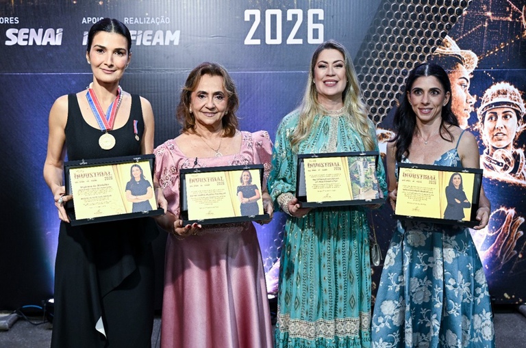 Foto mostra quatro mulheres segurando uma placa de reconhecimento tendo um painel ao fundo