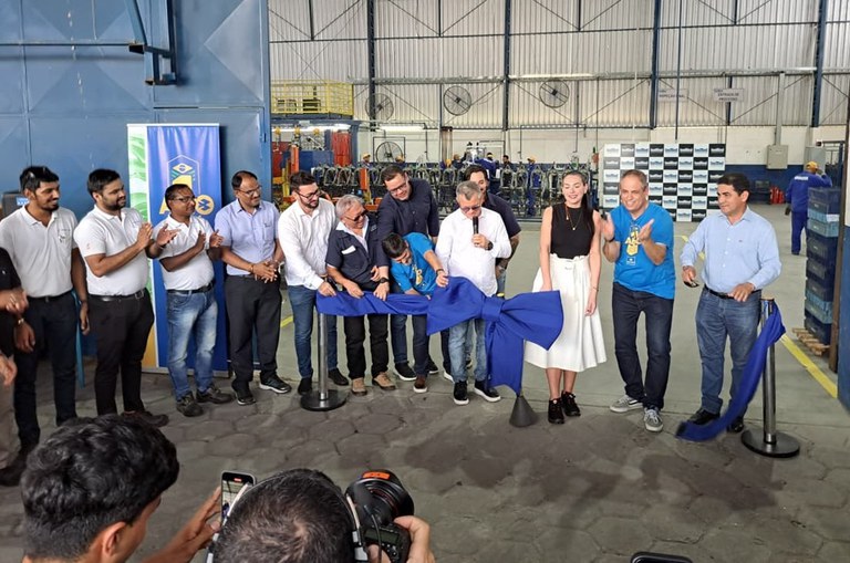 Foto mostra grupo de pessoas descerrando uma fita de inauguração numa fábrica