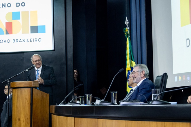 Foto mostra homem de blazer falando ao microfone