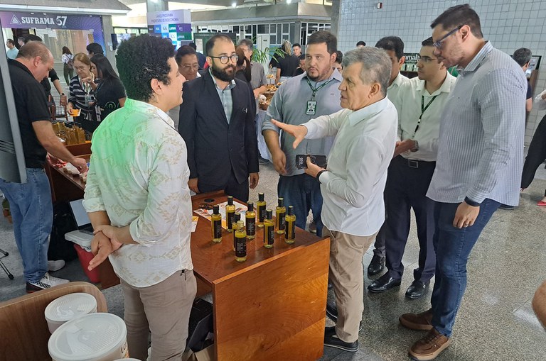 Foto mostra homem estendendo a mão e falando ao outros homens, num estande com produtos de vidro