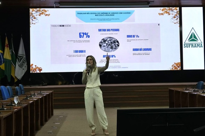 Foto mostra mulher falando ao microfone durante palestra com um telão ao fundo