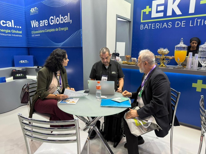 Foto mostra homem olhando para um notebook, obervado por outro homem e uma mulher