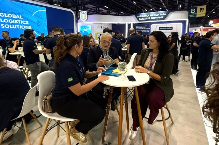 Foto mostra homem de óculos mostrando um informativo impresso a duas mulheres