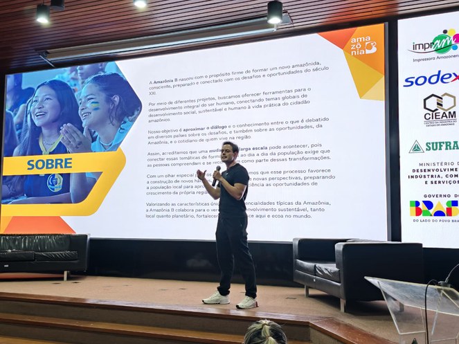 Foto mostra mulher ministrando palestra com telão ao fundo