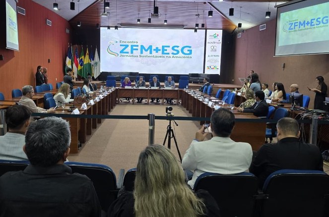 Foto mostra pessoas num auditório com um telão ao fundo