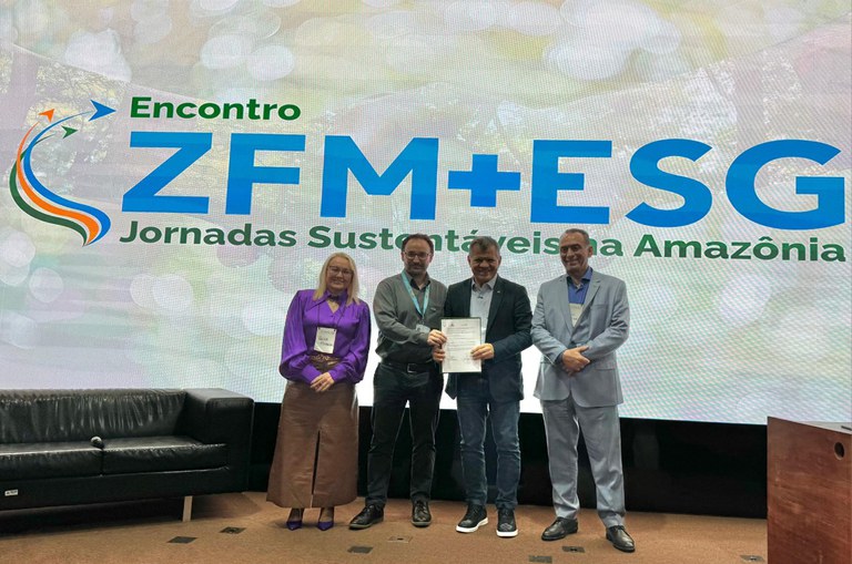 Foto mostra pessoas mostrando um documento, com telão ao fundo