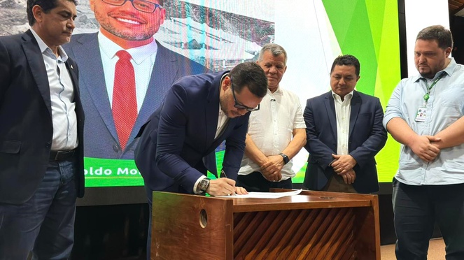 Foto mostra homem assinando documento, observado por outros homens