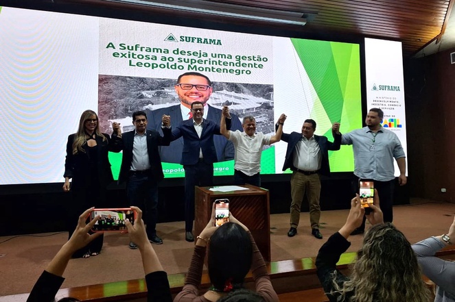 Foto mostra pessoas de mãos dadas em frente a um telão