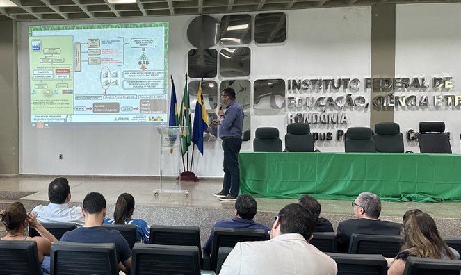 Foito mostra homem fazendo uma palestra num auditório, com o apoio de um telão