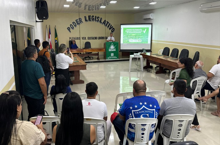 Foto mostra homem em pé falando num evento com microfone na mão 