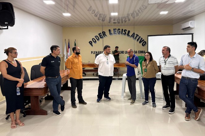 Foto mostra de blusa azul e sacola no braço falando a um grupo de pedsoas