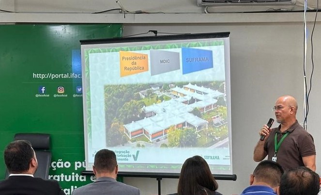 Foto mostra homem em pé ministrando um palestra, com telão como apoio