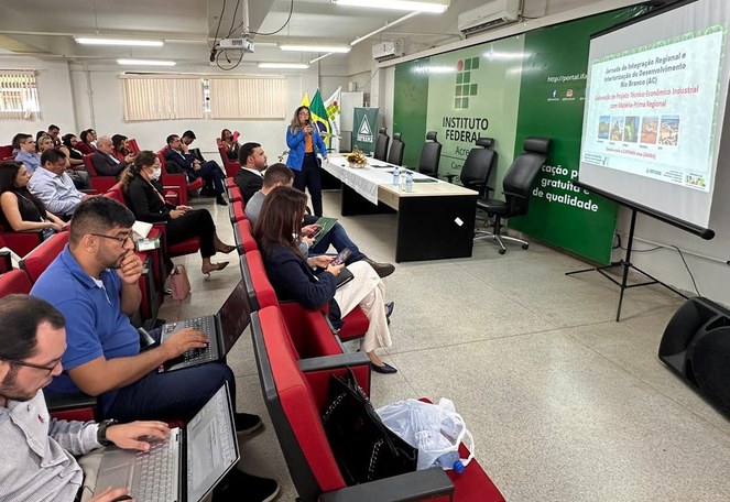 Foto mostra mulher em pé ministrando palestra com apoio de telão