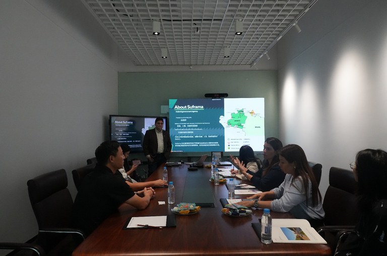 Pessoas sentadas ao redor de uma mesa com um palestrante de pé ao lado esquerdo