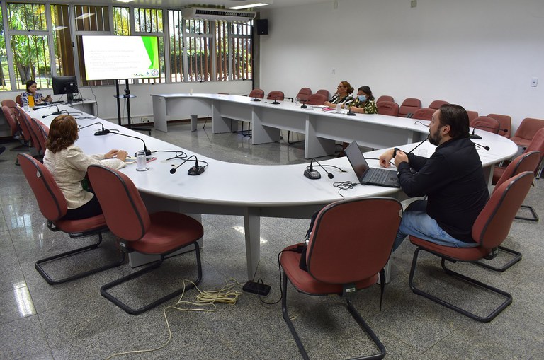 Foto mostra homem de barba falando ao centro da mesa em uma reunião virtual