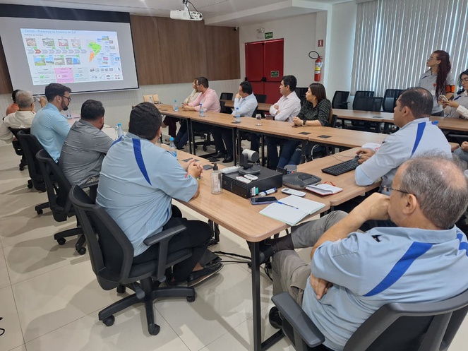 Foto mostra pessoas sentadas olhando para um telão